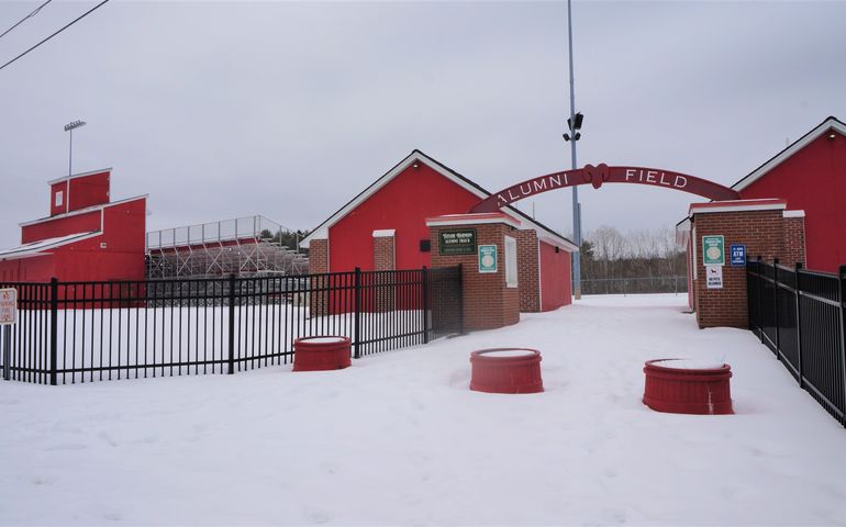 a bright red arched ticket booth that says alumni field with a red grandstand behind it, and snow on the ground