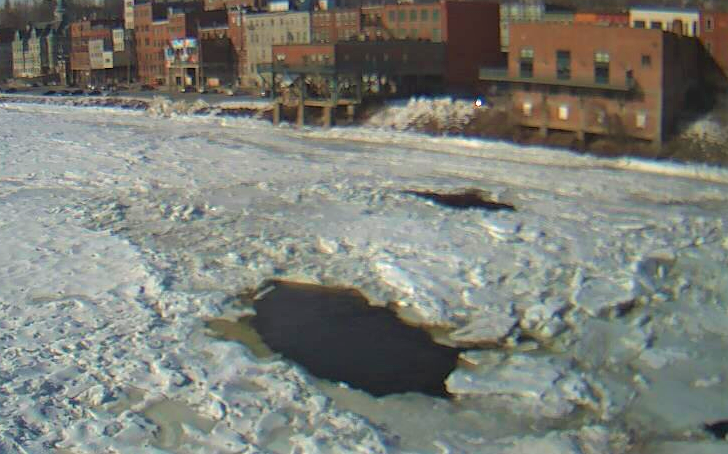 a frozen river with a downtown with brick buildings along the bank