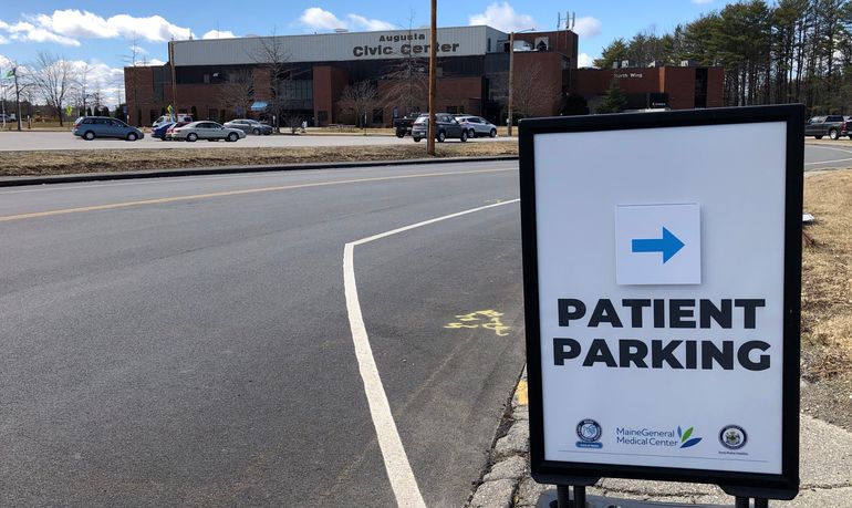 A large building with a sign that says augusta civic center is in the background with a closeup of a sign that says patient parking with an arrow there are scattered cars in the parking lot