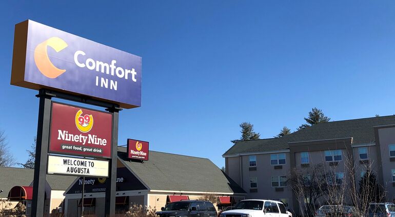 A sign says Comfort Inn and smaller 99 restuarant and below that welcome to Augusta, a restuarant and hotel building can be seen behind