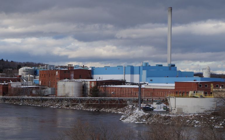 A multibuilding mill with a big smokestack on a river bank