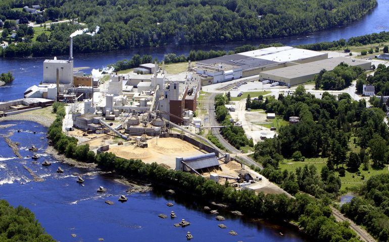 aerial view of large paper manufacturing plant, with stack, bordered by bright blue river