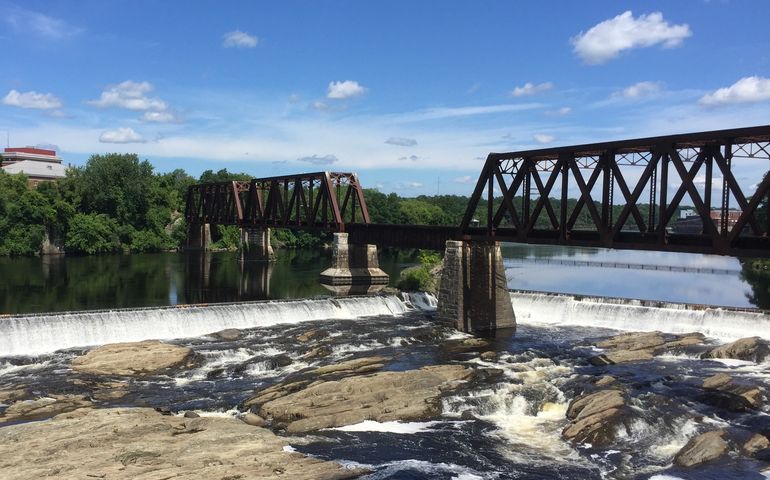 a river with rocky falls and a railroad bridge going over it