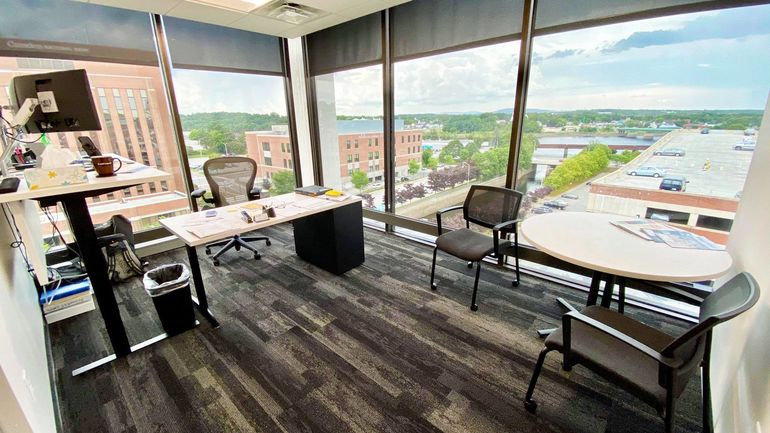 a modern looking office space with giant windows overlooking a small city with lots of old brick buildings