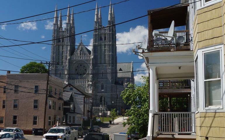 old triple decker housing lines  a street with a large gothic church on a hill bheind