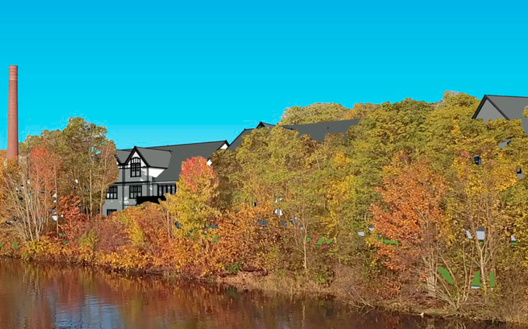 some tudor style roof tops peak out from behind trees with water in the forebround. a brick smokestack can be seen in the back