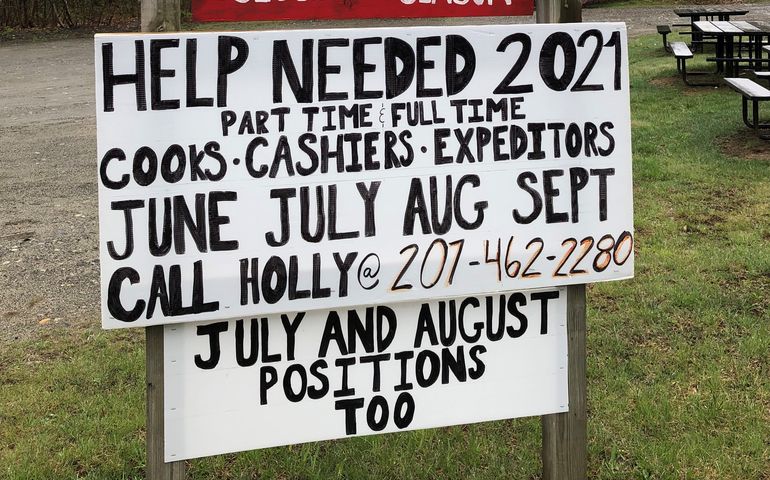 A sign says help needed for 2021 cooks cashiers expediters with a phone number