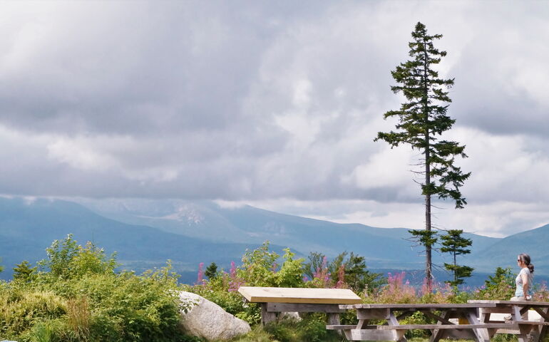 an overlook with picnic tables looking towards mountains with clouds at the tops