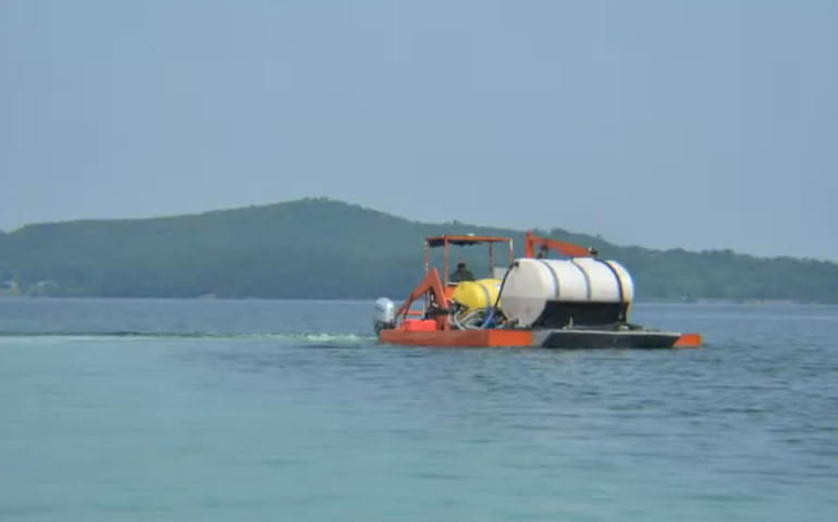 a boat with a large tank on a blue lake with hills in the background