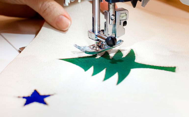 Close up of a Maine flag being sewn, showing hand of sewer and machine