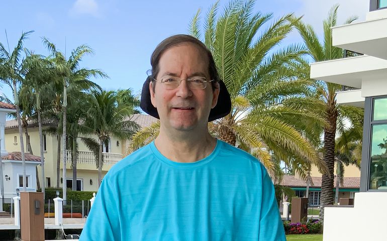 Jonathan Ayers among palm trees (head rest from wheelchair visible), in Florida.