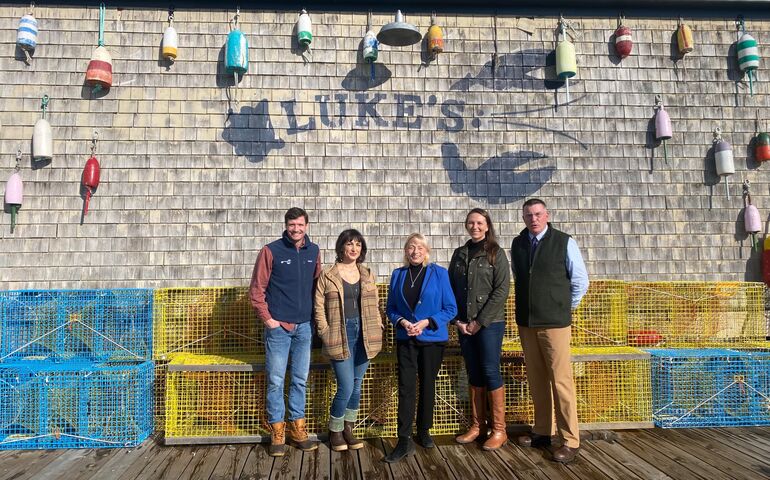 Gov. Mills and five other people outside Luke's Lobster on the Portland waterfront; lobster crates are behind them.