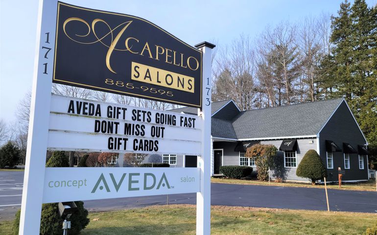 white wooden sign with "Acapello Salons" in front of gray one-story building