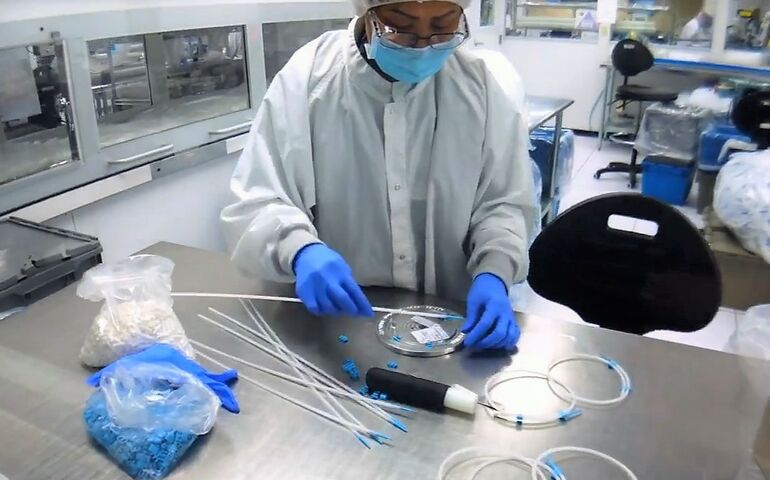 worker in mask and gown working to assemble wires on metal desk