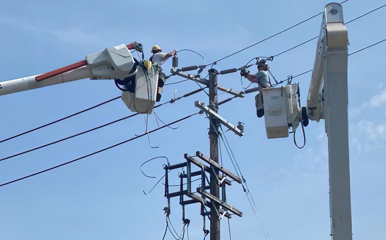 Utility workers working on power lines against a blue-sky backdrop.