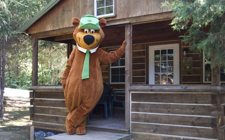 Yogi Bear leaning against a wood cabin door 