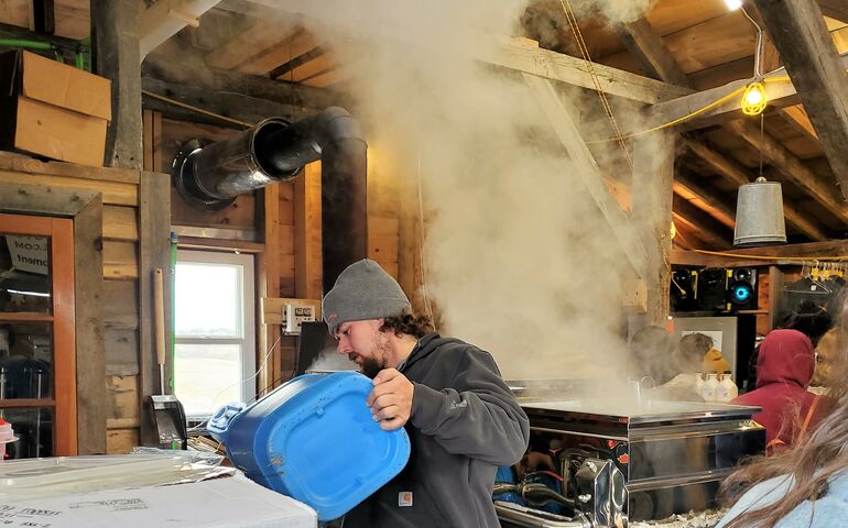 man pouring liquid into an industrial tank, near a machine billowing steam