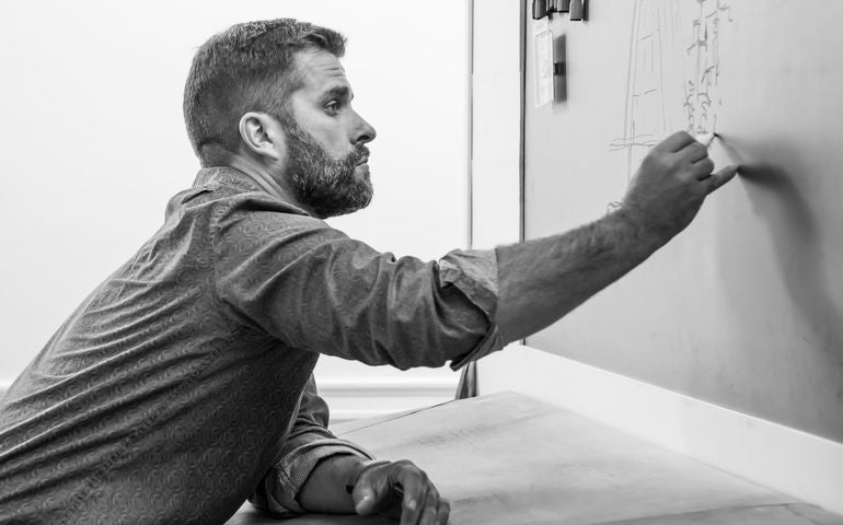 black and white photo of person leaning over writing on board