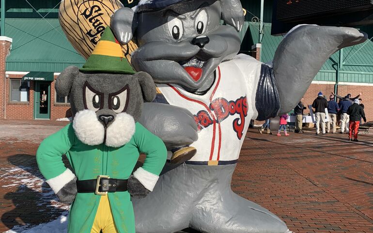Slugger in an elf outfit, standing next to Slugger statue outside Hadlock Field