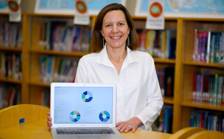 Kippy Smith seated, holding laptop that shows her app on the screen 