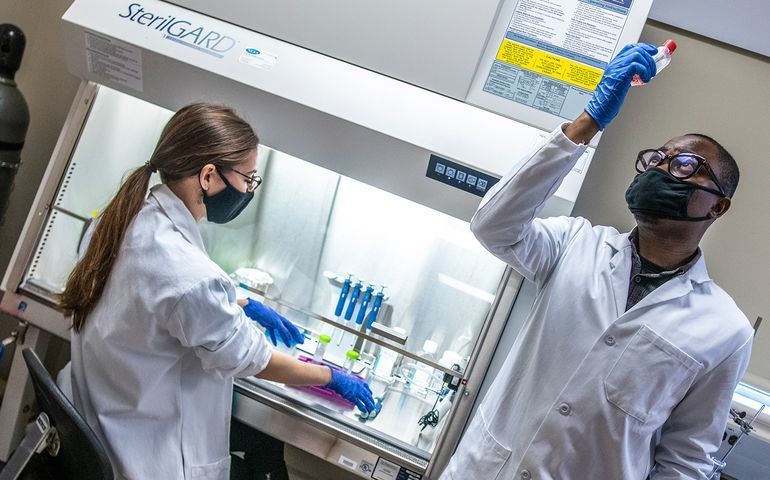 2 people in masks and lab coats with test tubes