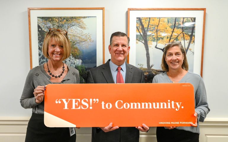 three people holding orange sign "YES!" to Community.