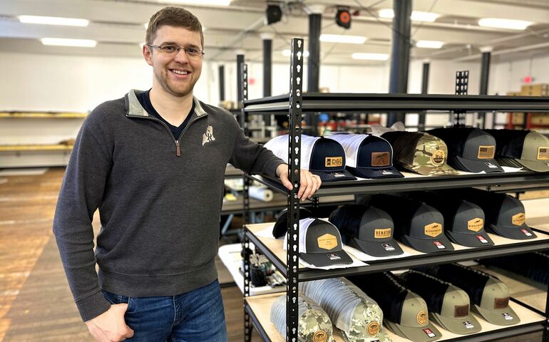 person smiling and standing with rack of hats