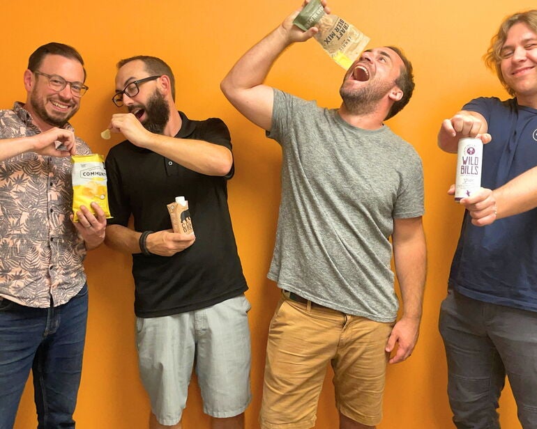 4 people standing with orange wall and acting goofy