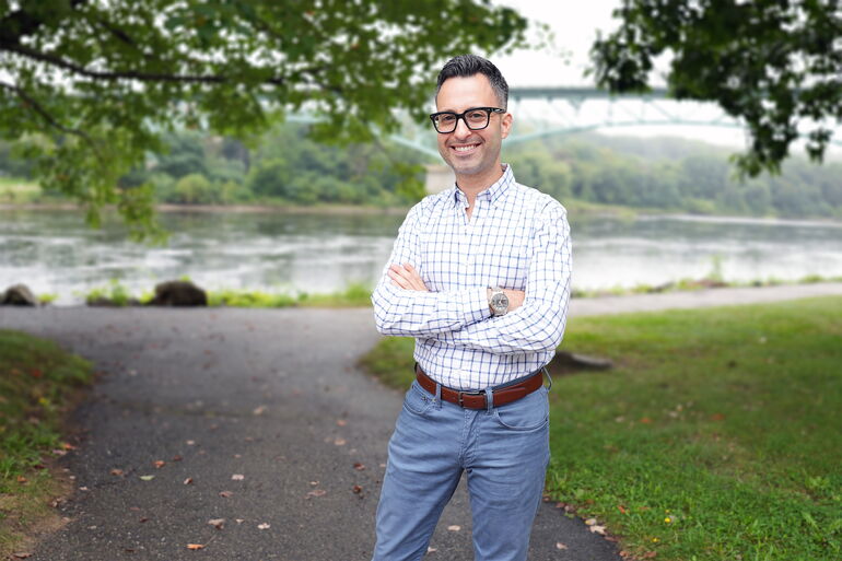 person in checked shirt and glasses by river smiling