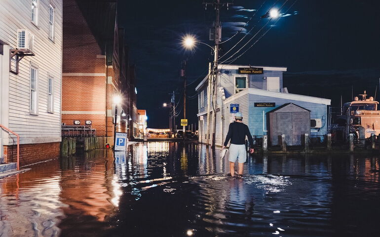 person walking at night through knee-high water with buildings and streetlights