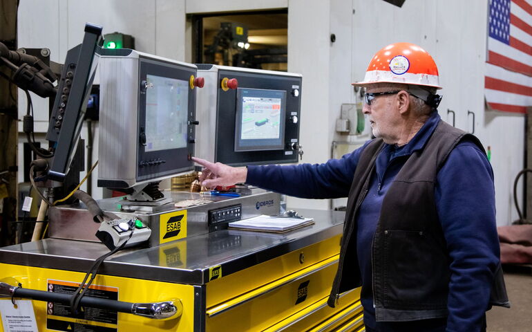 person in hardhat at computer monitor and machinery