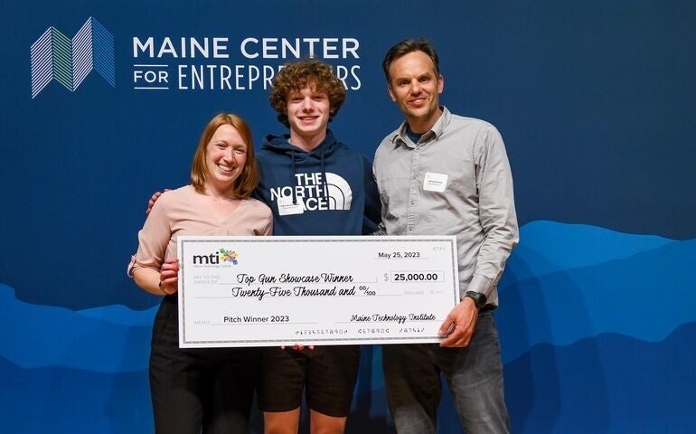 3 people with oversize check standing in front of sign