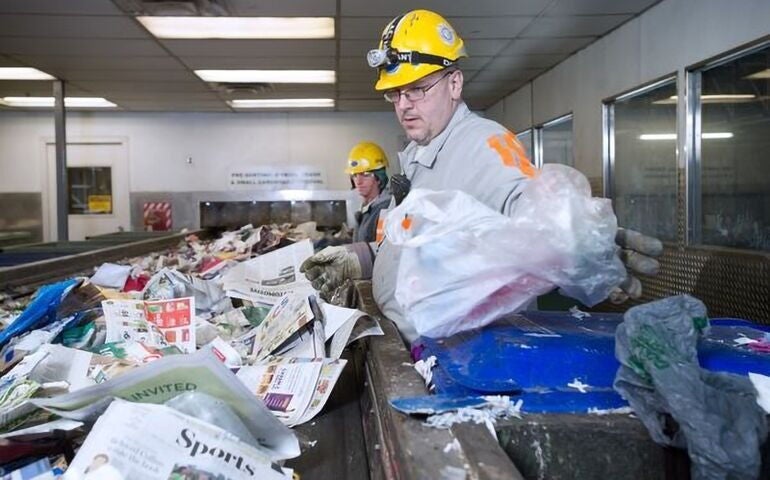 2 people in yellow hardhats with paper trash on conveyor belt