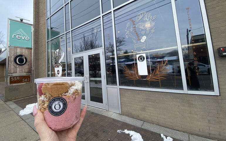 Hand holding smoothie in front of storefront 