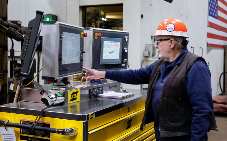 person in hardhat at computer monitors and machinery