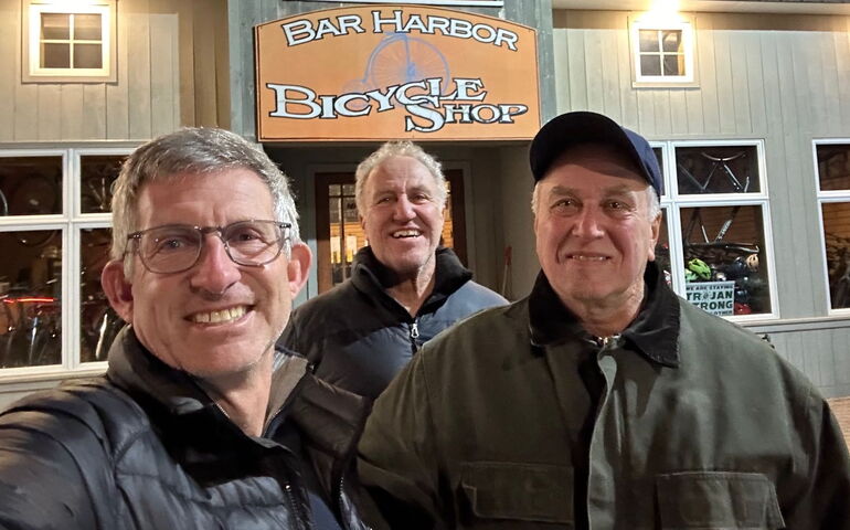 3 people in front of shop with sign