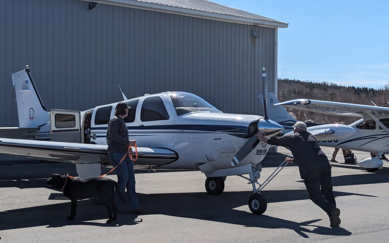 A small plane being pushed by a man while another man holds a leash on a dog.