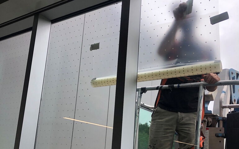 At LLBean, a person stands outside a window applying a film of bird-safe decals.