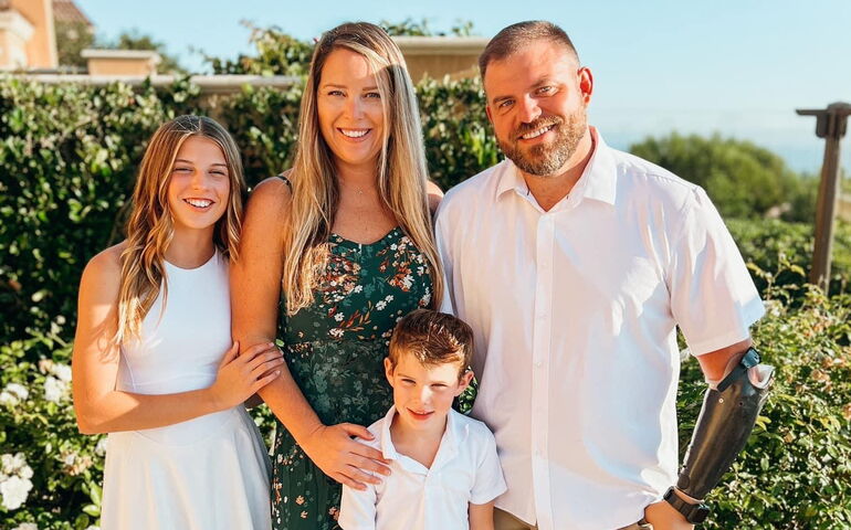 four people posing and smiling in front of bushes