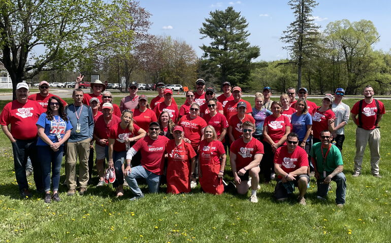 A  group of people, many wearing red T-shirts, pose on the grass either standing or kneeling.