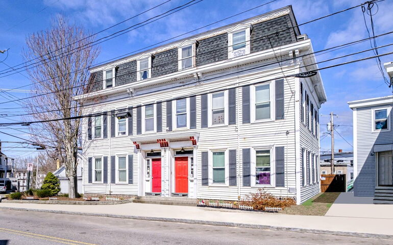 Street view of an old white sided building with two red doors.