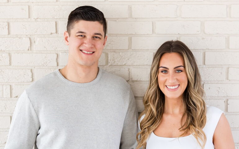 Two people with Maine Home Watch pose against a white-painted brick wall.