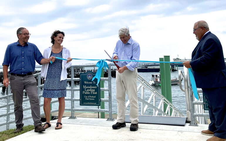 Four people cut a blue ribbon near the water.