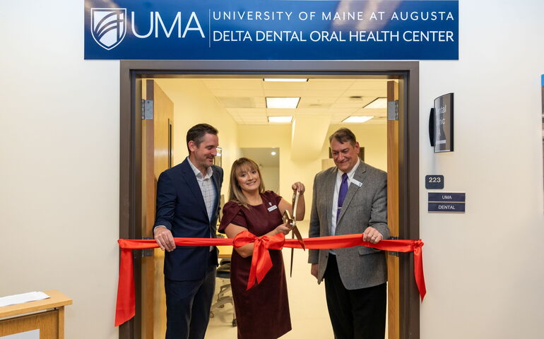 One person cuts a red ribbon while two others look on.