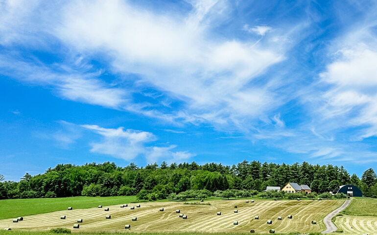 A view of the sky and plowed fields with hay.