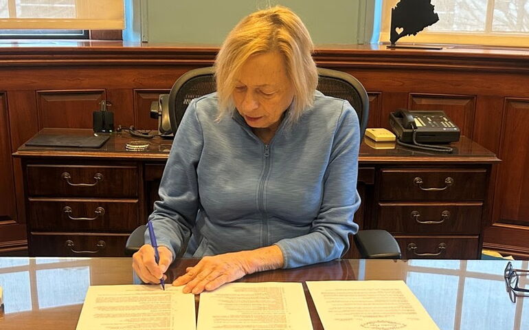 Janet Mills signing paper at a table or desk.