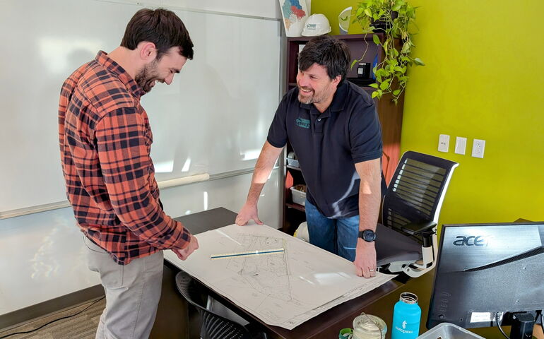 Two people stand at a drafting table.
