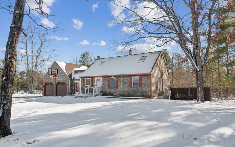 A cedar-shingled house is surrounded by a snowy lawn.