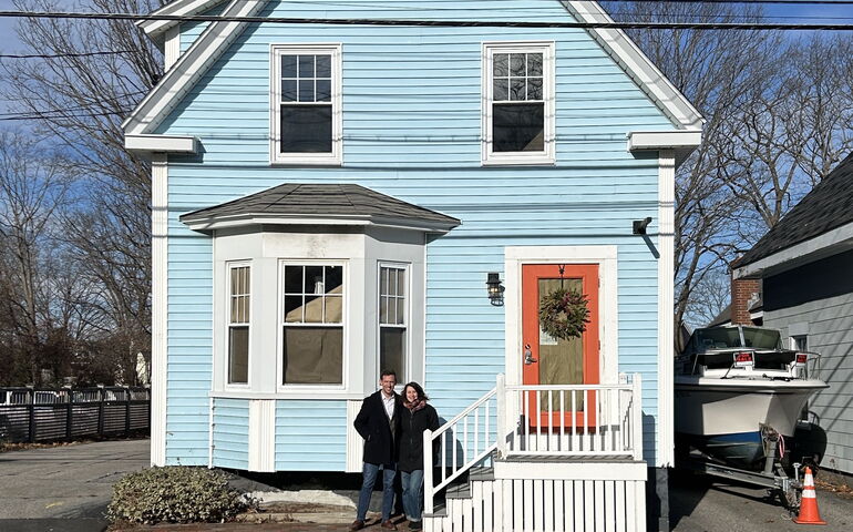 Two peole pose outside a blue building with a red door.