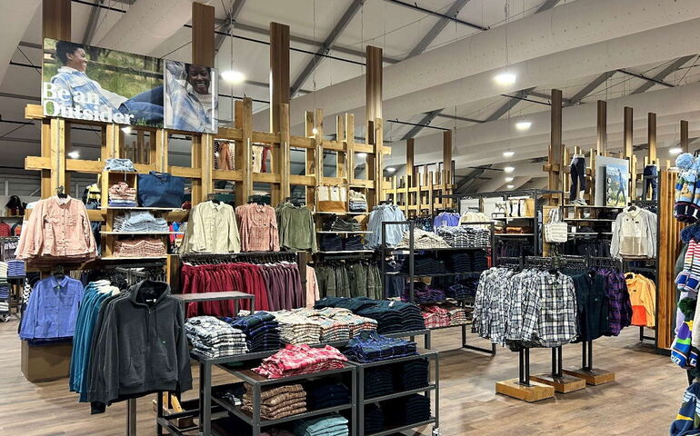 A store interior has racks and shelves full of clothes.